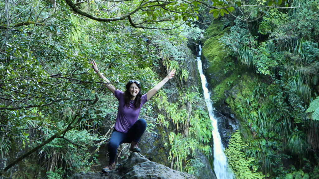 Travel vlogger posing next to waterfall. 
